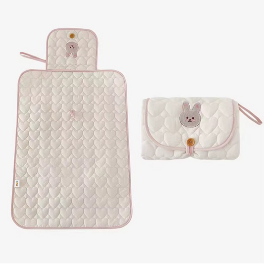 Pink foldable quilted baby changing pad and matching folded pad with rabbit face design.