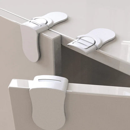 Close-up of white baby safety locks on cabinet door edges showing locking mechanism.