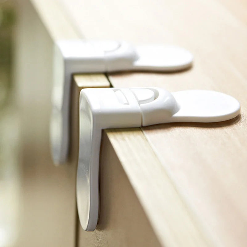 Two white baby safety locks attached to wooden cabinet edges side view.