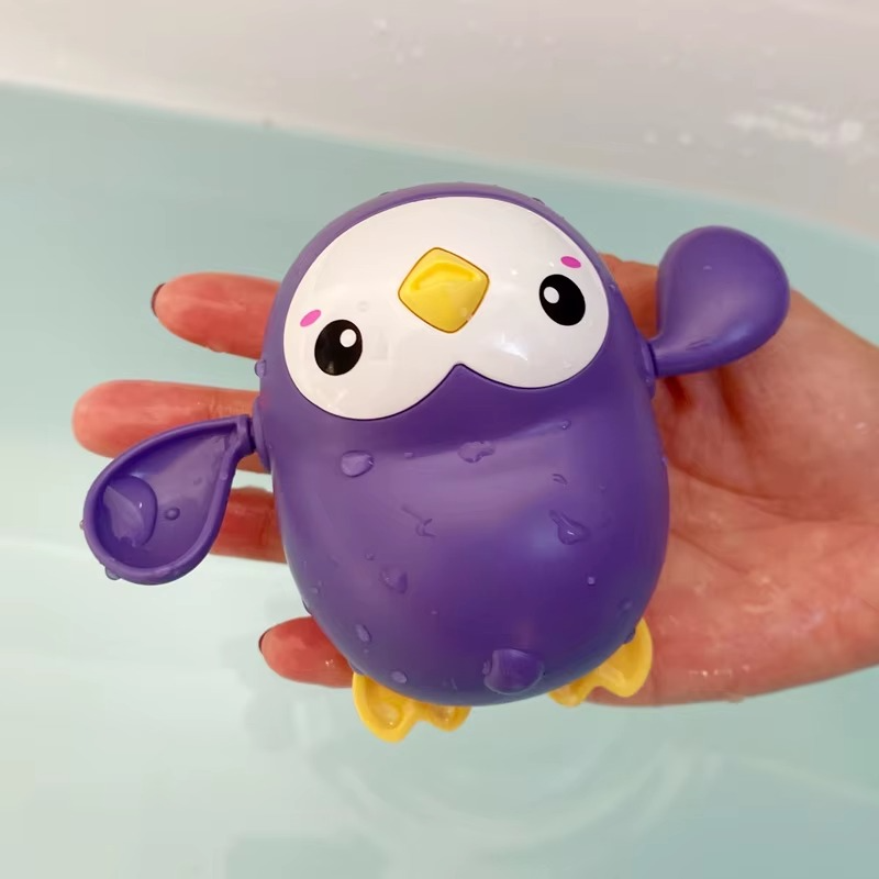 Purple penguin wind-up bath toy with yellow beak and feet held over water.