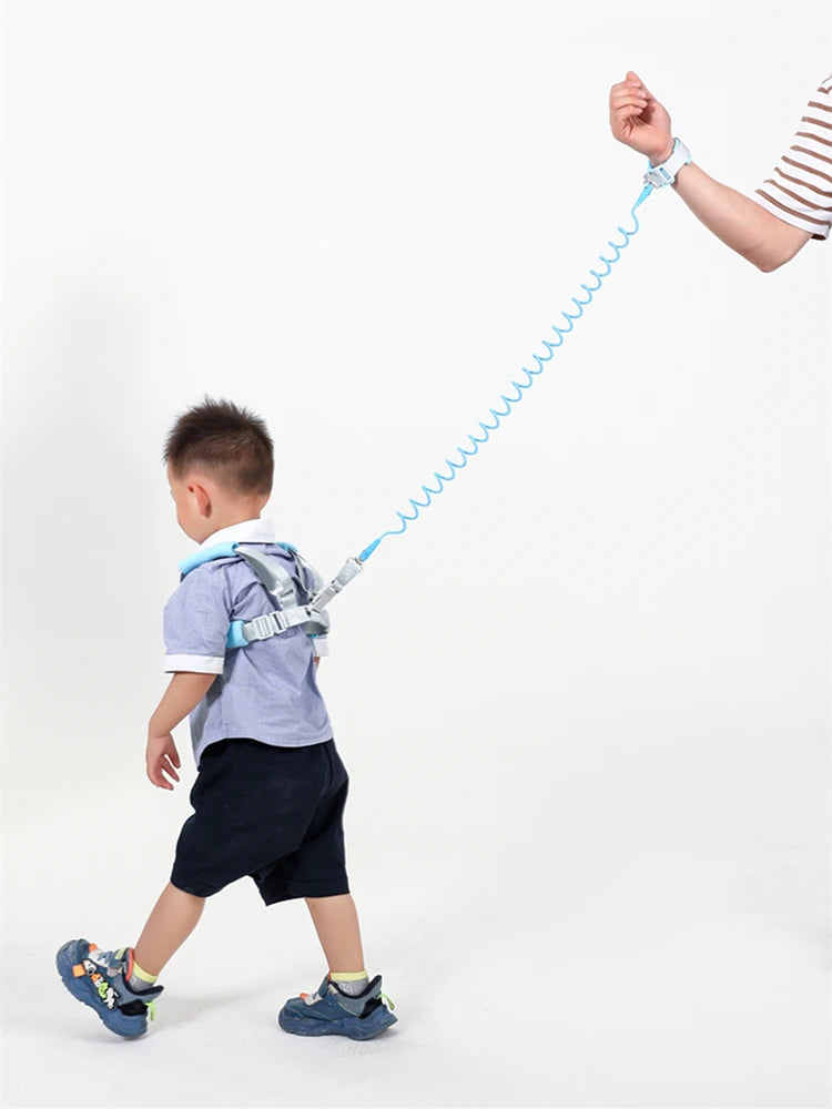 Side view of toddler wearing blue anti-lost safety harness with spring leash wrist strap held by adult.