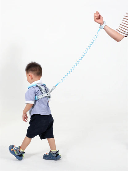 Side view of toddler wearing blue anti-lost safety harness with spring leash wrist strap held by adult.