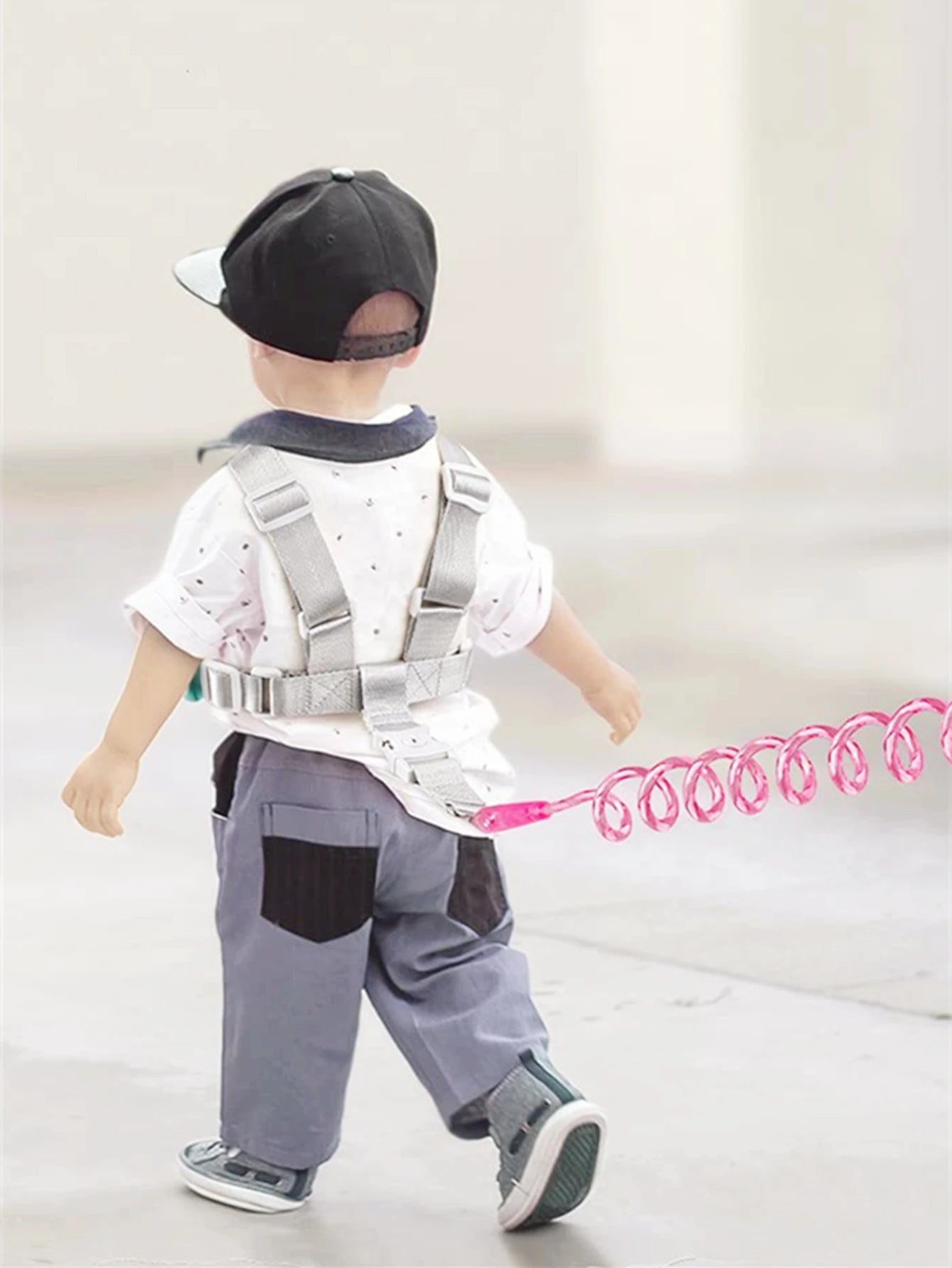 Toddler wearing pink anti-lost safety harness with spring leash walking outdoors.