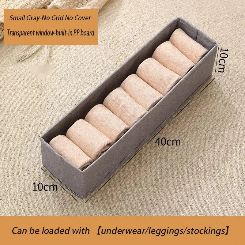 Small gray foldable fabric storage box with clear window for baby clothes storage.