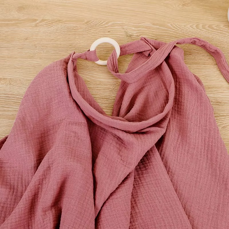 Close-up of dark pink breathable muslin nursing cover fabric and wooden ring adjustable strap.