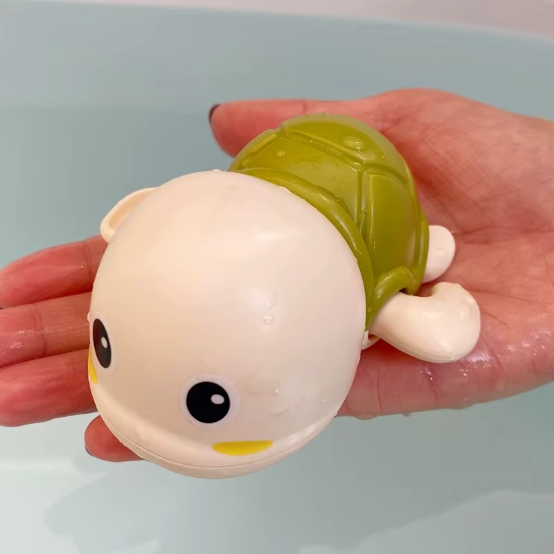 Hand holding white and green tortoise wind-up bath toy with water droplets.