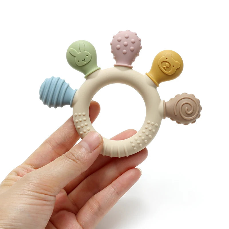 Hand holding pastel silicone baby teething ring showing textured chew heads and ring.