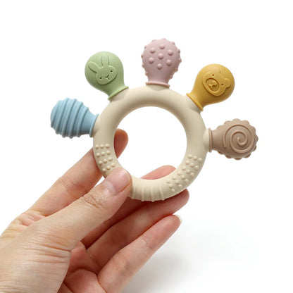 Hand holding pastel silicone baby teething ring showing textured chew heads and ring.