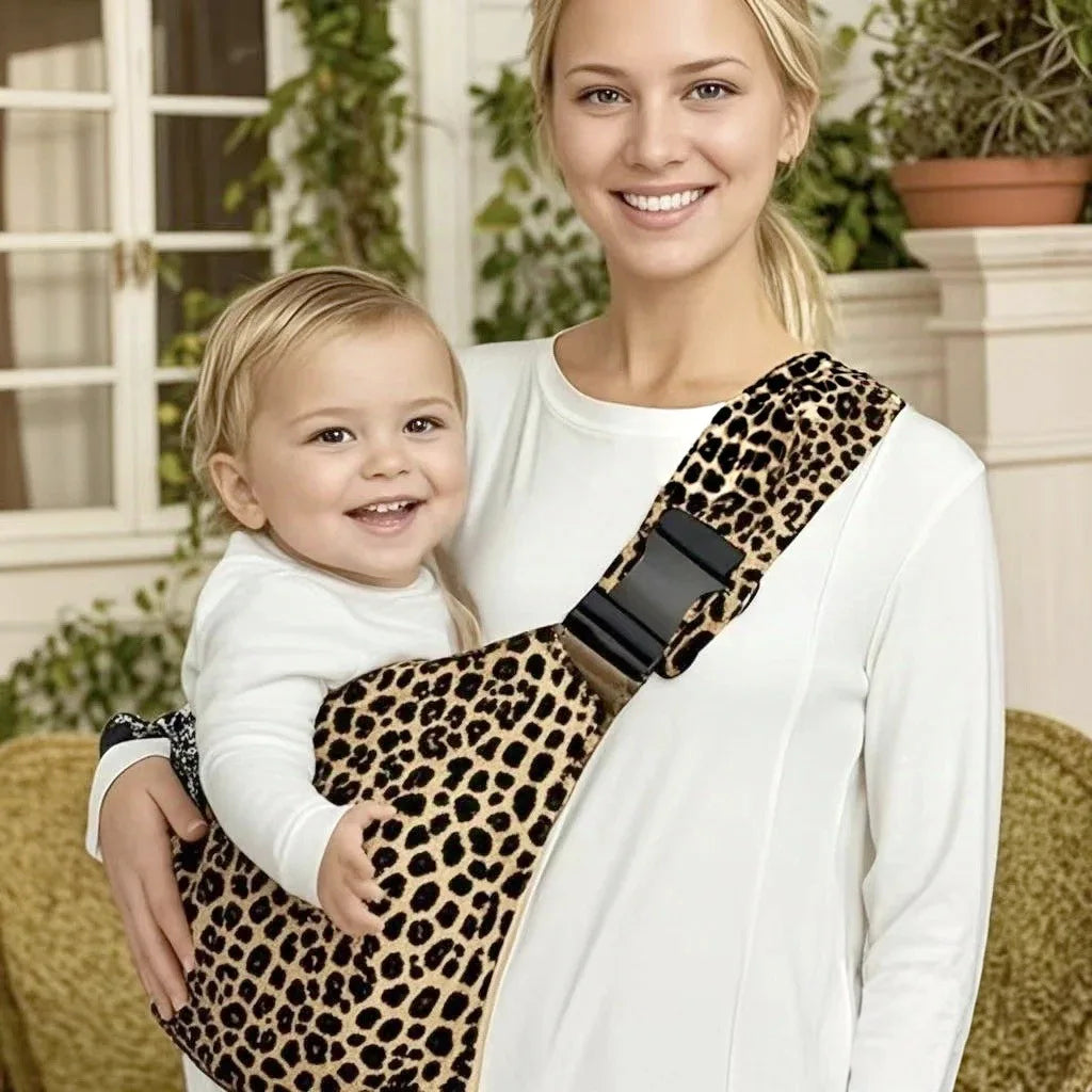 Leopard print adjustable baby carrier wrap worn sling style with baby held by woman.
