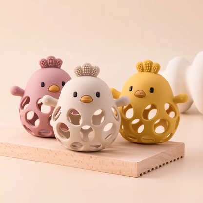 Silicone baby teether rattles in dusty pink, beige, and mango yellow on wooden board.