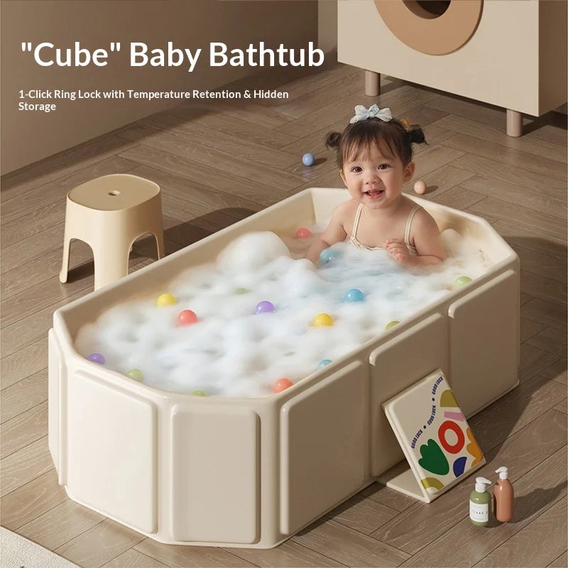 Cream foldable baby bathtub with foam and colorful balls, toddler inside, on wooden floor.