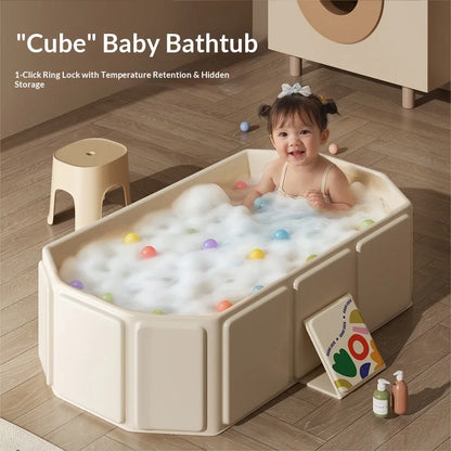 Cream foldable baby bathtub with foam and colorful balls, toddler inside, on wooden floor.