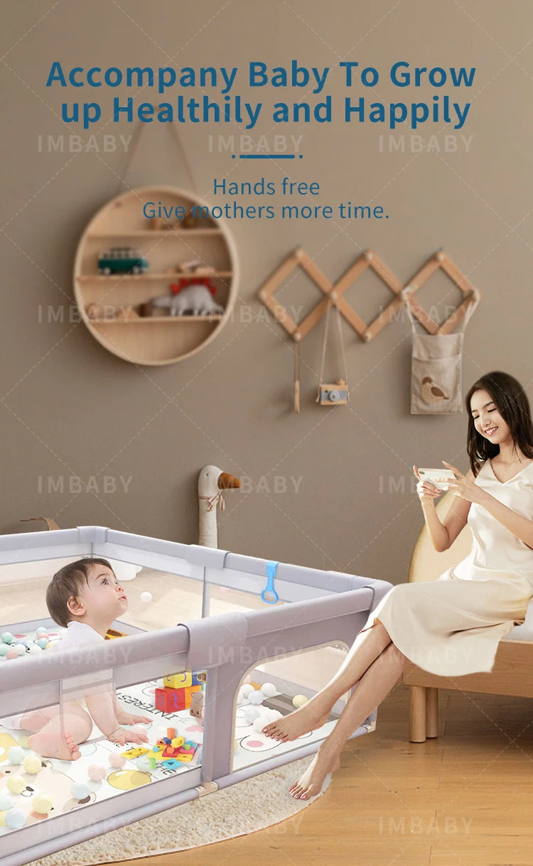Gray baby playpen with pull rings and baby playing, mother sitting nearby hands-free.