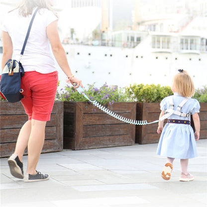 Adult holding spring leash connected to toddler wearing blue anti-lost safety harness outdoors.