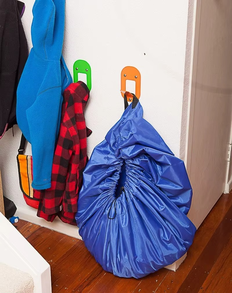 Blue portable toy storage play mat bag hanging on wall hook in hallway with coats.