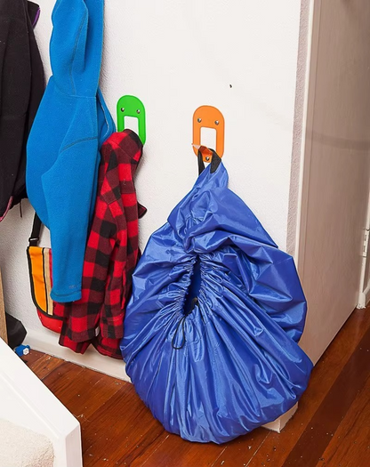 Blue portable toy storage play mat bag hanging on wall hook in hallway with coats.