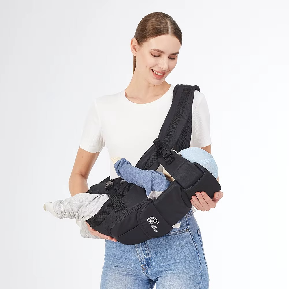Black ergonomic baby carrier used as hands-free sling holding baby horizontally.