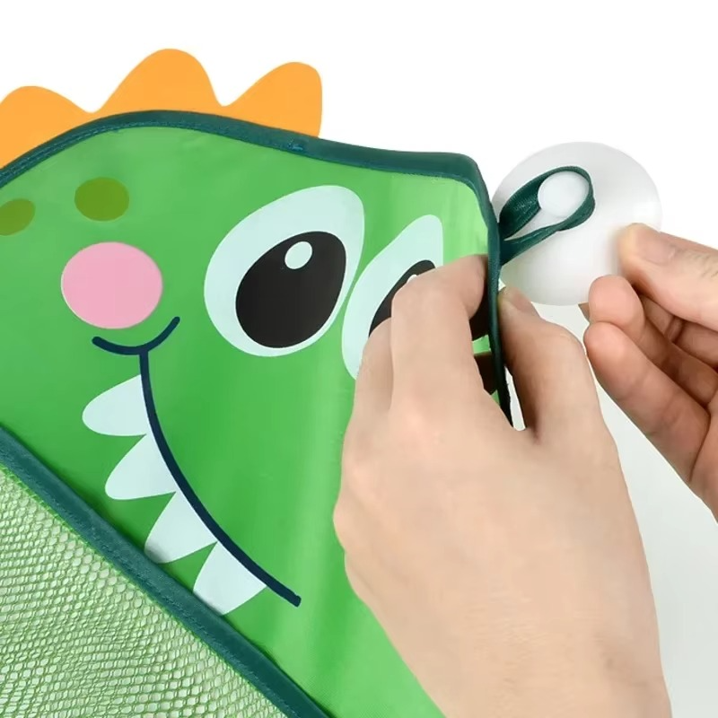 Hands attaching suction cup to green dinosaur bath toy storage mesh bag corner.