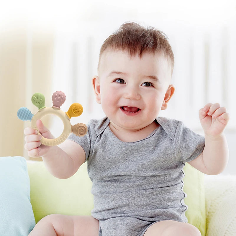 Baby holding pastel silicone baby teething ring with five textured chew heads.