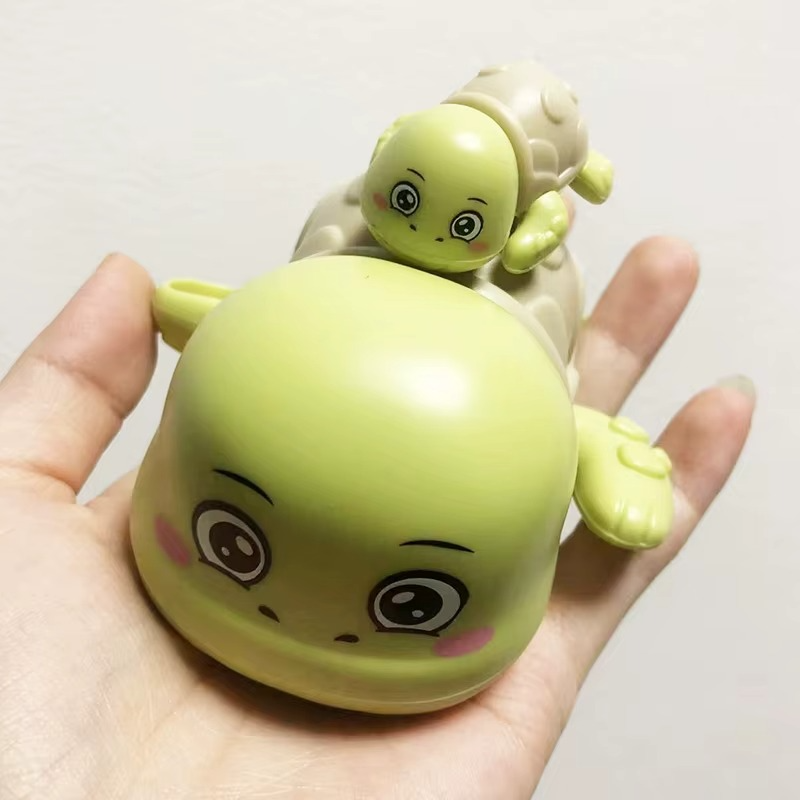 Hand holding green tortoise wind-up bath toy with smaller tortoise on back.
