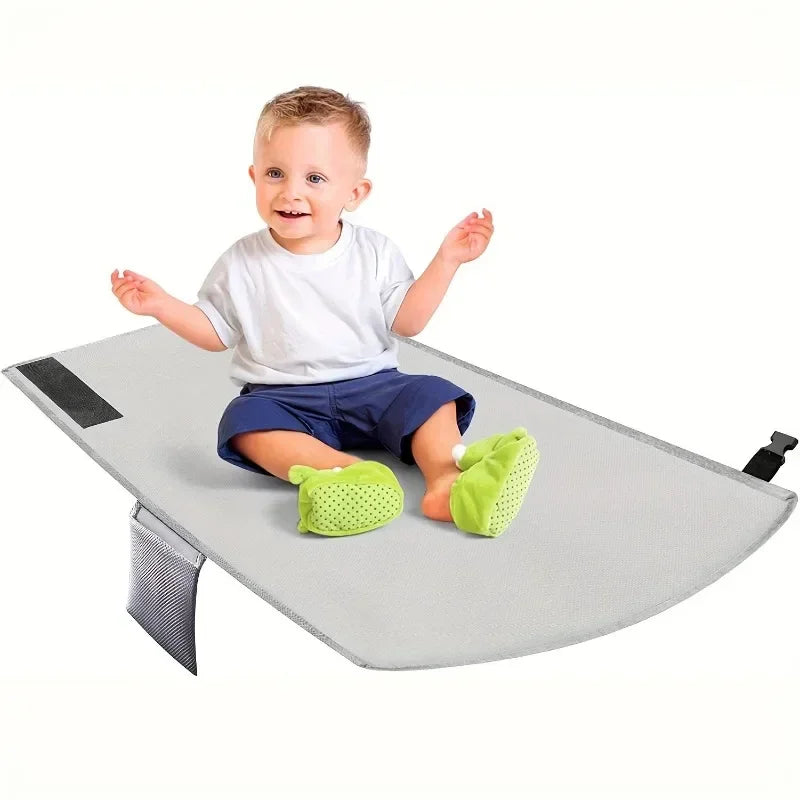 Toddler sitting on gray kids airplane foot hammock with mesh side pocket.