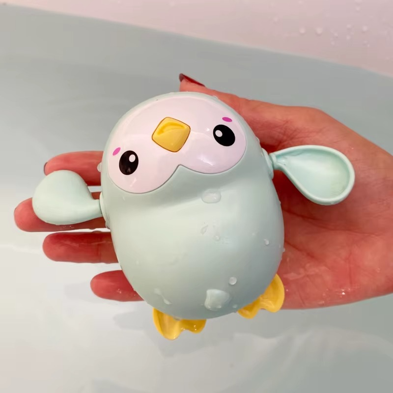 Green penguin wind-up bath toy with yellow beak and feet held over water.