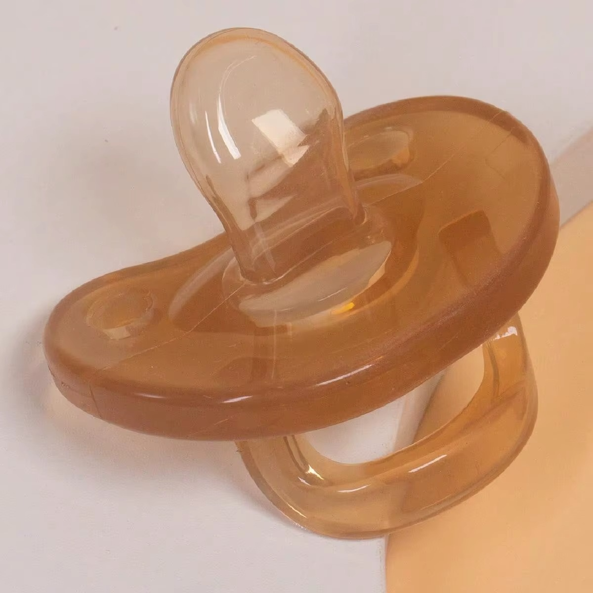 Close-up of light brown silicone baby pacifier with flat nipple and handle.