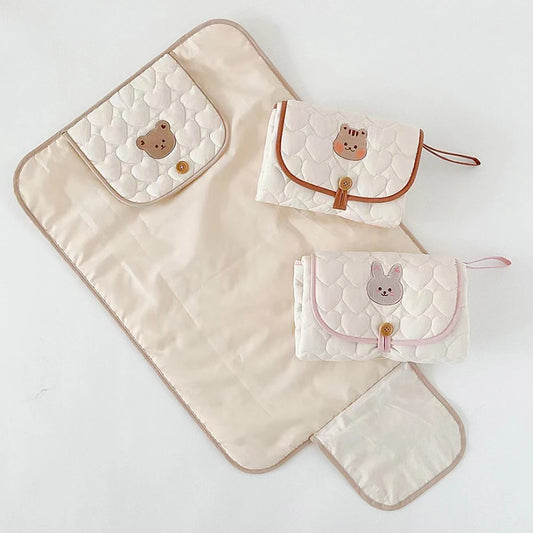 Foldable quilted baby changing pads in beige with bear, tiger, and rabbit animal designs.