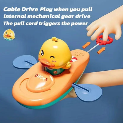 Hand pulling red cord on yellow duck kayak bath toy demonstrating wind-up cable drive.