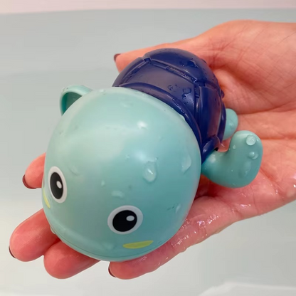 Hand holding blue tortoise wind-up bath toy with water droplets.