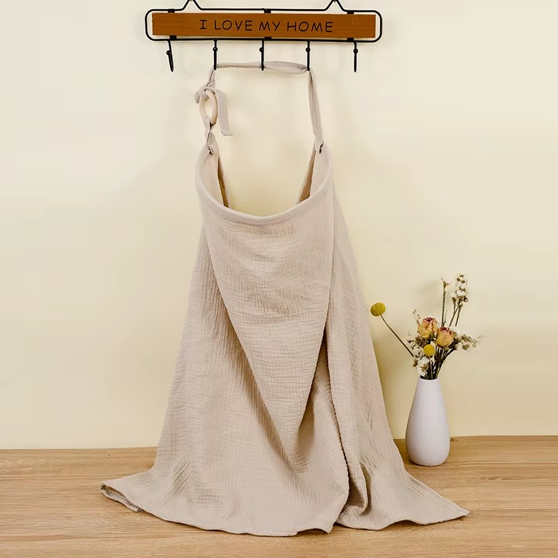 Khaki breathable muslin nursing cover hanging on hook with adjustable strap.
