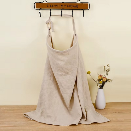 Khaki breathable muslin nursing cover hanging on hook with adjustable strap.