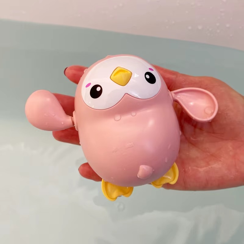 Pink penguin wind-up bath toy with yellow beak and feet held over water.