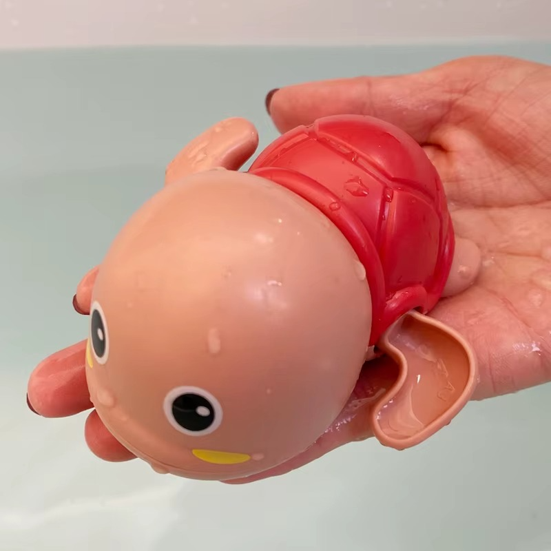 Hand holding red tortoise wind-up bath toy with water droplets.