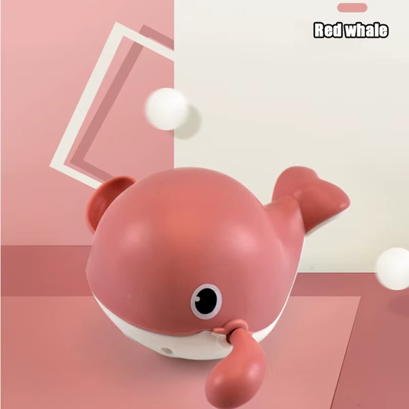Red whale wind-up bath toy on pink geometric background.