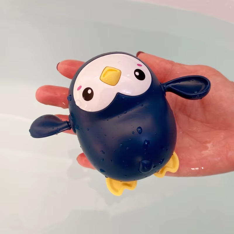 Blue penguin wind-up bath toy with yellow beak and feet held over water.
