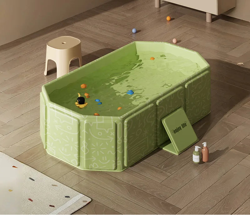 Green foldable baby bathtub filled with water and colorful balls on wooden floor with bath products.