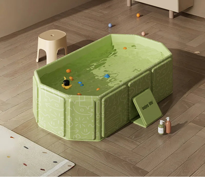 Green foldable baby bathtub filled with water and colorful balls on wooden floor with bath products.