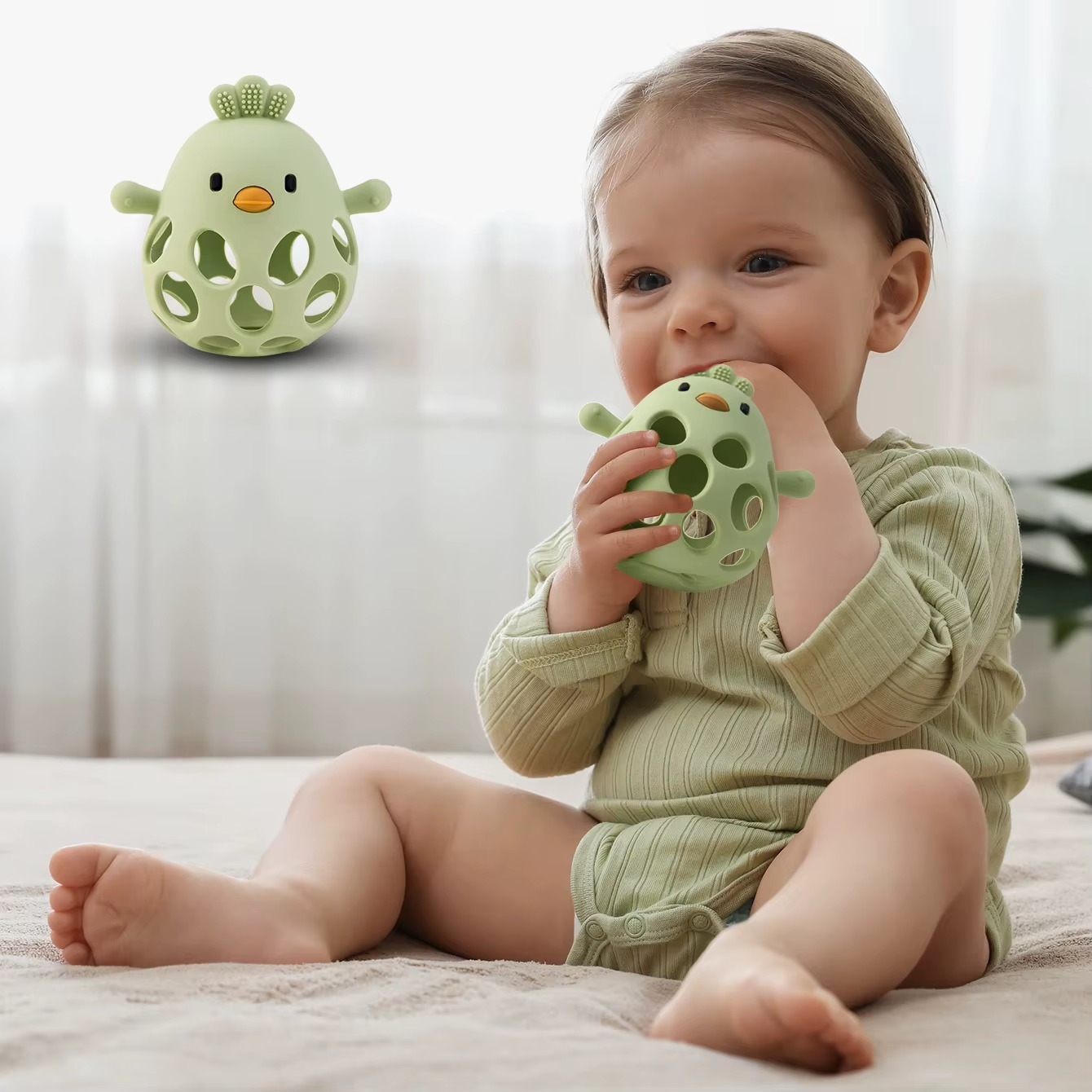 Baby holding olive green silicone baby teether rattle while sitting on floor.