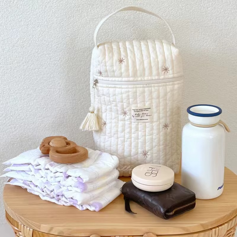 Snowflake quilted diaper caddy bag with embroidered stars and front zipper pocket on wooden table with baby essentials.