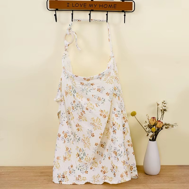 Floral breathable muslin nursing cover hanging with adjustable strap and wooden ring.