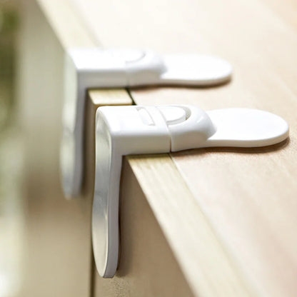 Side view of white baby safety locks attached to light wood cabinet edges.