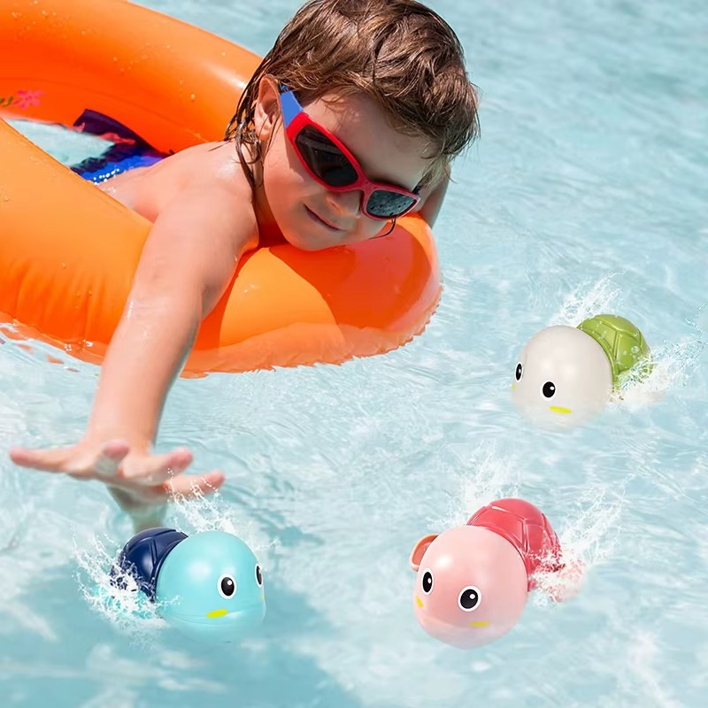 Child reaching for three colorful wind-up turtle bath toys swimming in pool.