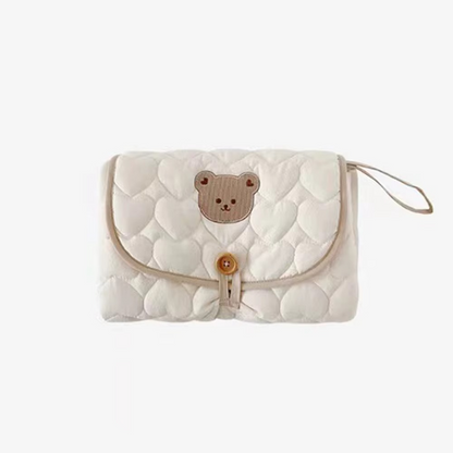 Beige foldable quilted baby changing pad folded with bear face design on flap.