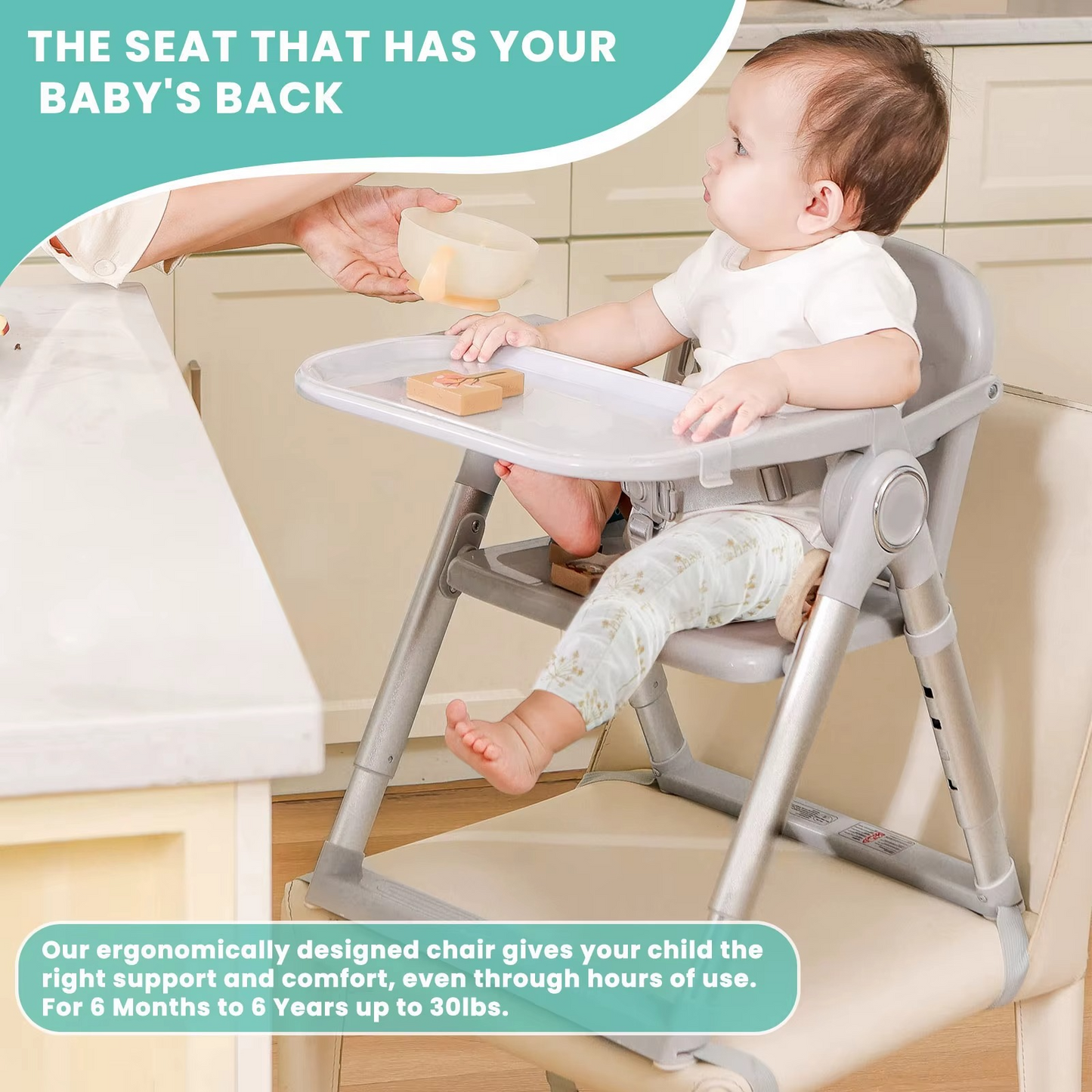 Baby seated in gray portable booster seat with tray, feeding time in kitchen.