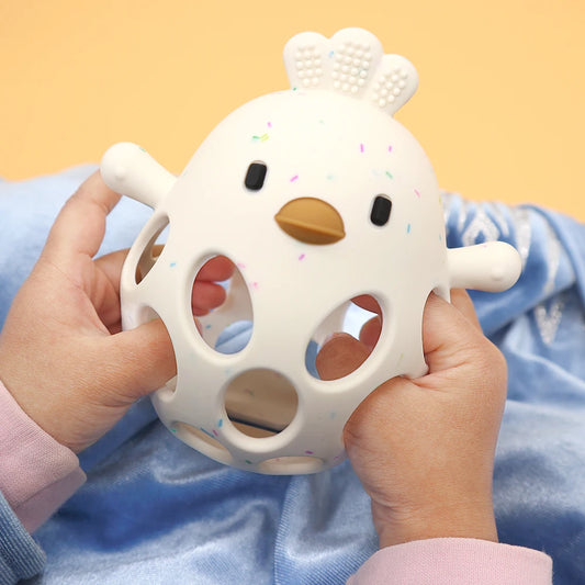 White silicone baby teether rattle with colorful speckles held by hands.